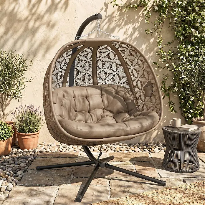 Outsunny Hängesessel - L x B x H: 126 x 126 x 176 cm, Sand, Schwarz - Brauner Hänge-Eiersessel im Rattan-Stil mit weichem taupefarbenem Kissen und schwarzem Ständer auf einer sonnigen Terrasse.