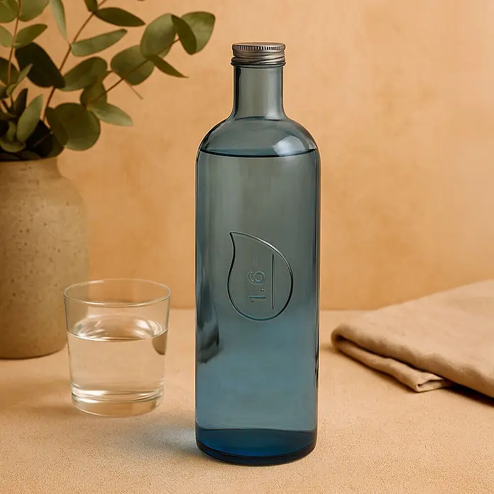 Versa Botella gota agua - 1,6 l, Vidrio, Azul - Botella de agua de cristal azul con tapón metálico, llena de agua, junto a un vaso.