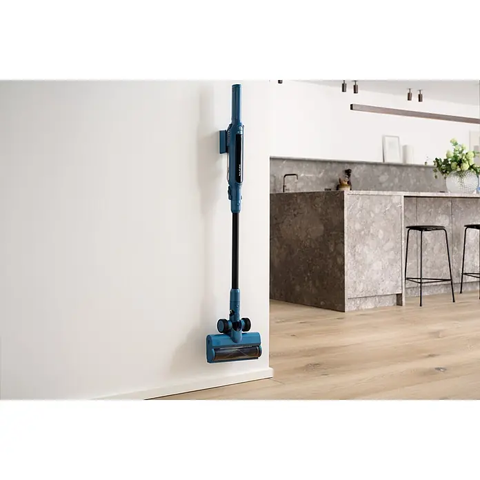 Nilfisk Aspirador de batería Move - 150 W, Volumen de recipiente: 0,2 l, Negro, Con soporte de pared - Aspiradora escoba azul montada en una pared en una cocina moderna con suelo de madera.