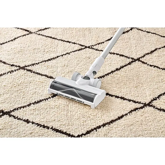 Nilfisk Aspirador de batería Move - 150 W, Volumen de recipiente: 0,2 l, Blanco, Con soporte de pared - Cabezal de aspiradora blanco y gris con cepillo visible, limpiando una alfombra crema texturizada con patrón de rombos oscuros.