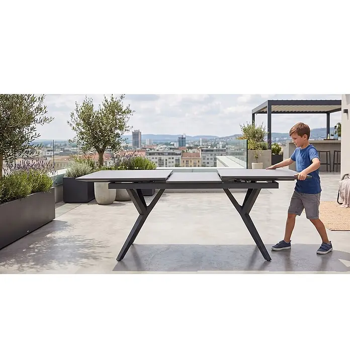 Bene Living Gartentisch Valor - L x B x H: 210 x 90 x 75 cm, Aluminium Gestell mit gesinnerter Tischplatte aus Keramik, Rechteckig, Anthrazit - Grauer ausziehbarer Outdoor-Esstisch wird von einem Kind auf einer modernen Terrasse eingestellt.