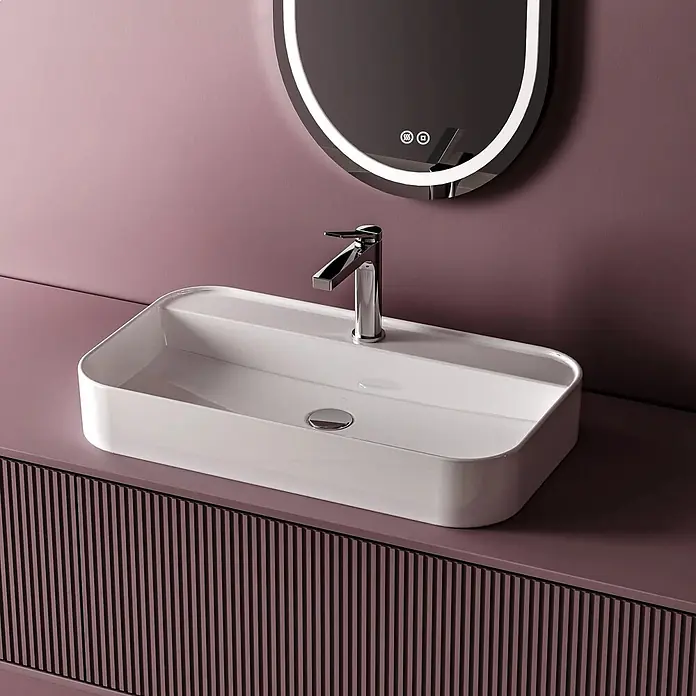 Emke Waschbecken Ceraform CB02 - Hahnloch: Mitte, Ohne Überlauf, Weiß - Weißes, rechteckiges Aufsatzwaschbecken mit Chromarmatur auf einem mauvefarbenen geriffelten Badmöbel, unter beleuchtetem Ovalspiegel, vor mauvefarbener Wand.
