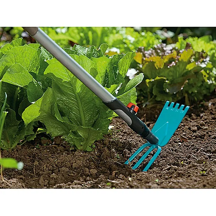 Gardena Combisystem Gartenhacke - Arbeitsbreite: 9 cm, Anzahl Zinken: 3, Stahl - Nahaufnahme einer blauen GARDENA-Gartenkralle, die in der Erde eines Gartens mit Salatköpfen verwendet wird.