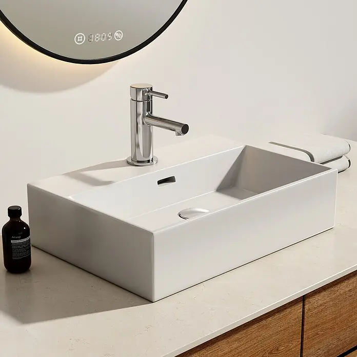 Emke Waschbecken Ceraedge CB01 - Hahnloch: Mitte, Mit Überlauf, Weiß - Ein weißes Aufsatzwaschbecken mit Chromarmatur auf heller Marmorplatte, neben einer Aesop-Flasche und Handtüchern, unter einem Smart-Spiegel.