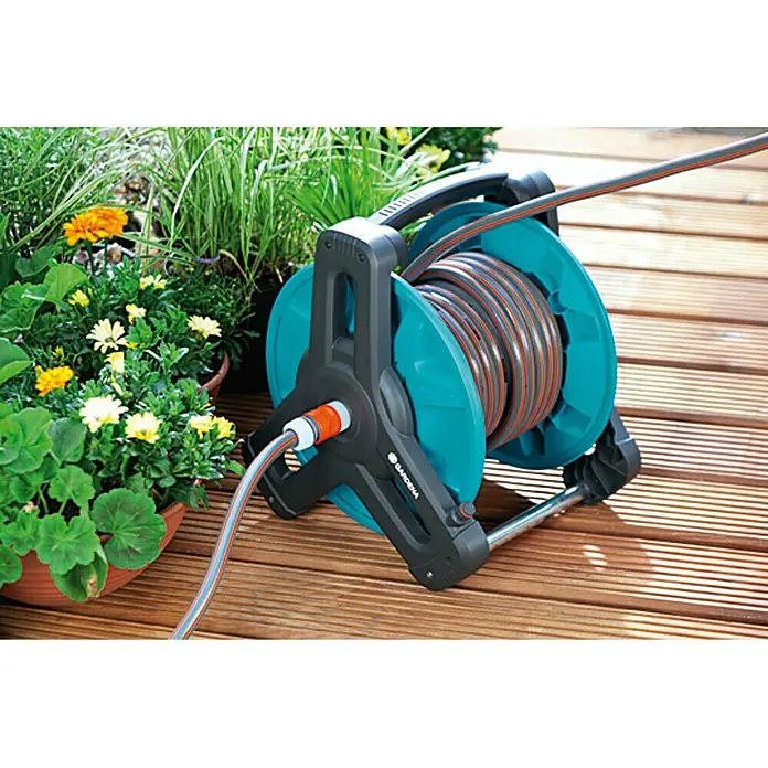 Gardena Classic Schlauchtrommel 50 - Kunststoff, Schlauchkapazität: 50 m, 13 mm (½″) - Eine Gardena Schlauchbox mit aufgerolltem Gartenschlauch steht auf einer Holzterrasse neben Blumen.