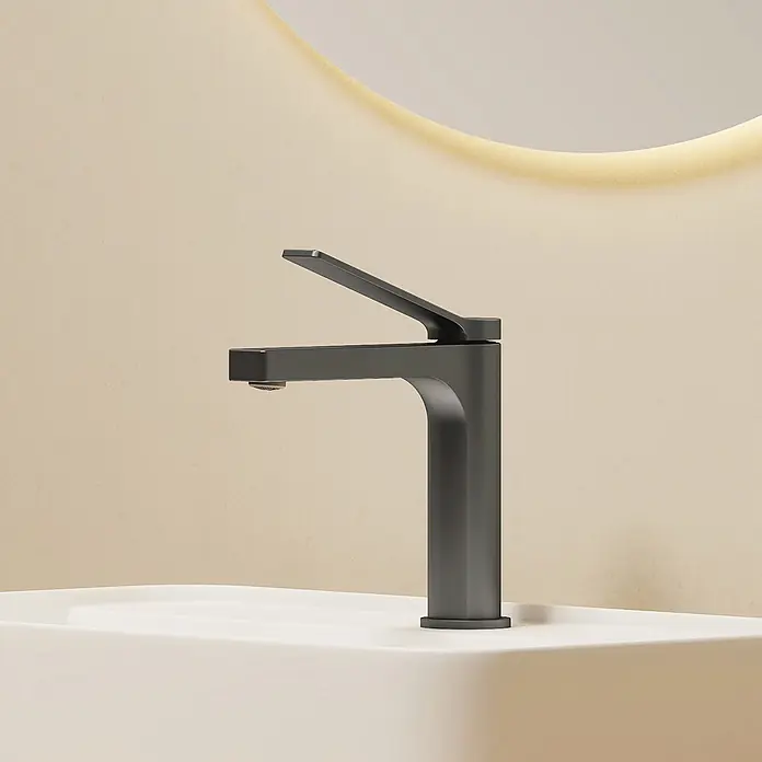Emke Waschtischarmatur Arcspout XF21 - Grau, Matt - Moderner mattschwarzer Wasserhahn auf einem weißen Waschbecken, vor einer hellbeigen Wand mit leuchtendem Spiegel.