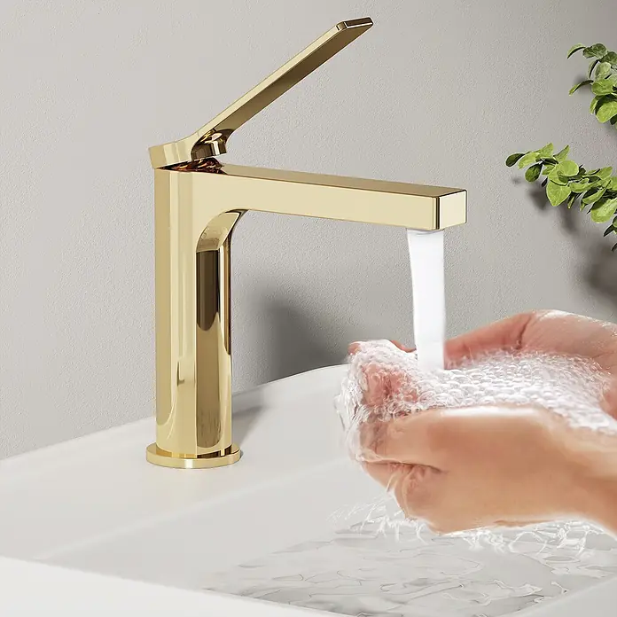 Emke Waschtischarmatur Arcspout XF21 - Gold, Glänzend - Polierter goldener Wasserhahn mit fließendem Wasser in gewölbte Hände, die Schaum im weißen Waschbecken bilden.
