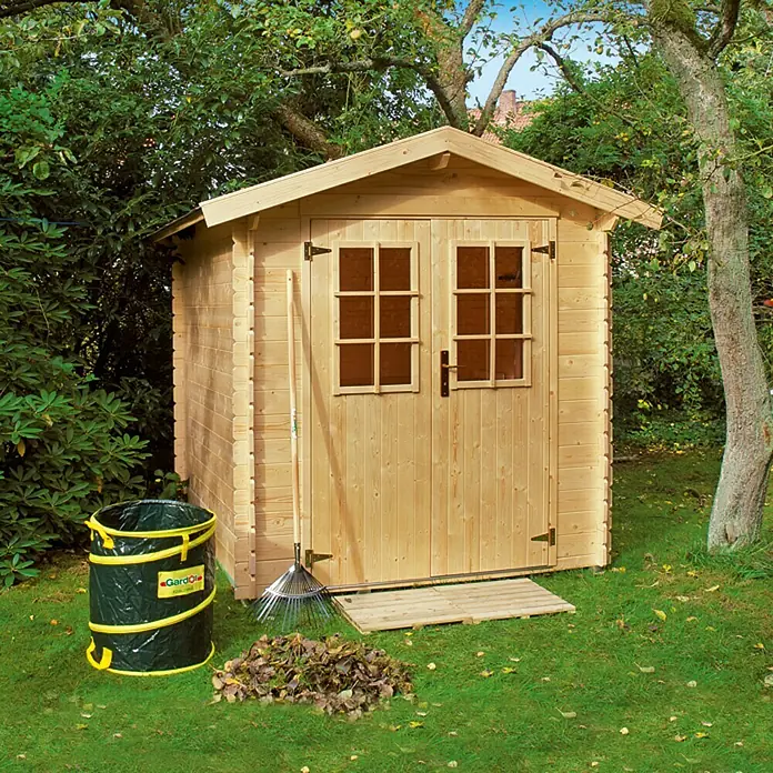 Kiehnholz Caseta de jardín Mikka - Medidas ext. (An x Pr): 228 x 233 cm, Madera, Natural, Tejado a dos aguas - Escena de jardín con una caseta de madera, una bolsa para hojas y un rastrillo, listos para jardinería.