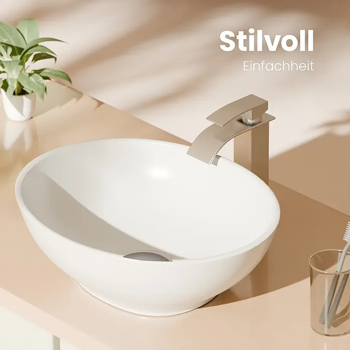 Emke Aufsatzwaschbecken Bovelari CB05 - 33,5 x 41,5 cm, Hahnloch: Ohne, Ohne Überlauf, Weiß - Weißes ovales Aufsatzwaschbecken und gebürsteter Metall-Wasserfallhahn auf hellem Waschtisch, mit Pflanze und Zahnbürste.