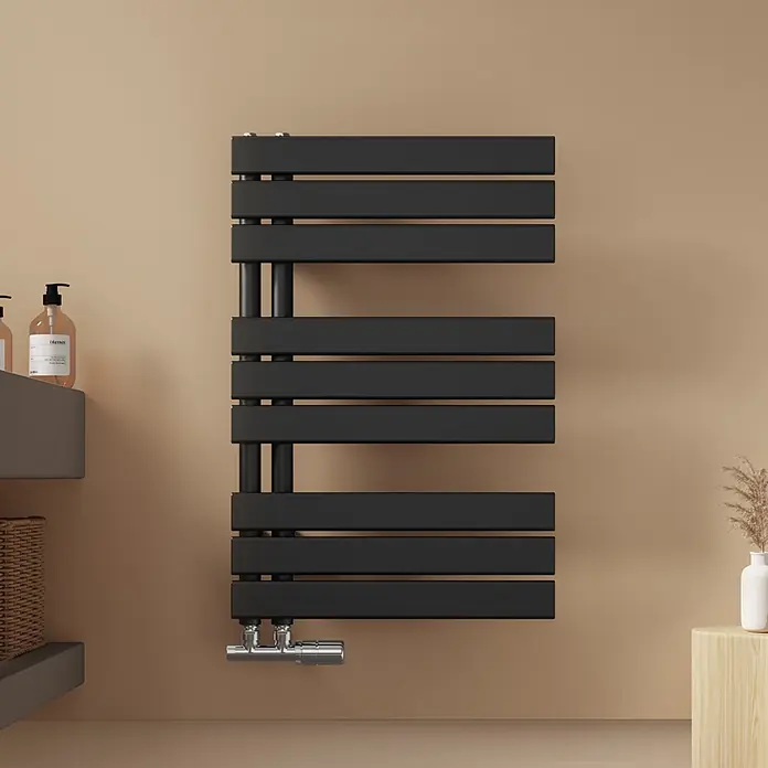 Emke Badheizkörper Flatrad SFTR1 - Schwarz - Schwarzer Flachrohr-Handtuchheizkörper an beiger Wand montiert, mit Chromarmaturen unten.