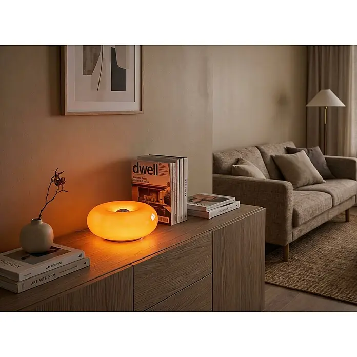 Eglo LED-Tischleuchte rund Basile - 8 W, Ø x H: 30 x 12 cm, Orange, Warmweiß - Eine leuchtende, orangefarbene Donut-Lampe auf einem Holzschrank, die warmes Licht in ein gemütliches Wohnzimmer wirft.