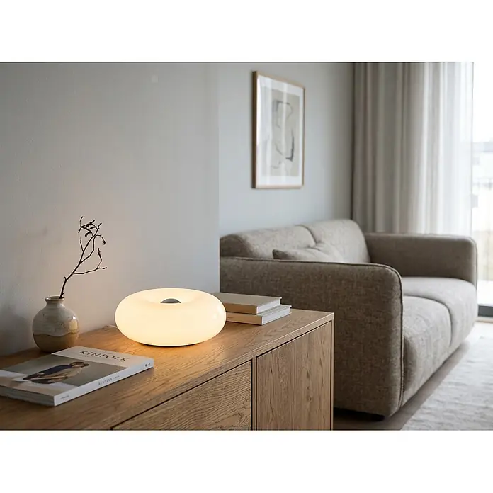 Eglo LED-Tischleuchte rund Basile - 8 W, Ø x H: 30 x 12 cm, Weiß, Warmweiß - Weiße, leuchtende, donut-förmige Tischlampe auf einem Holzschrank, die sanftes Umgebungslicht spendet.