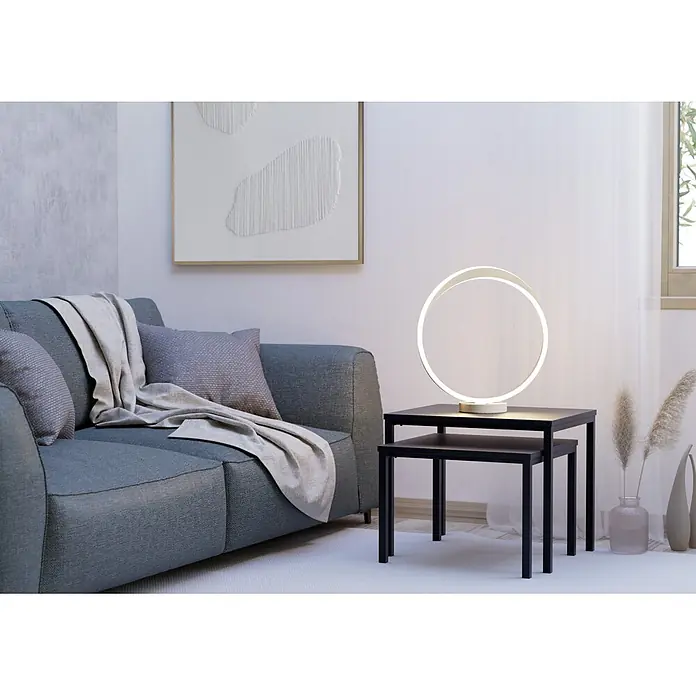 Eglo LED-Tischleuchte rund Camerota - 10 W, Ø x H: 40,5 x 44 cm, Sandfarben, Warmweiß - Eine beleuchtete, weiße ringförmige LED-Tischlampe steht auf einem dunklen Beistelltisch neben einem grauen Sofa.