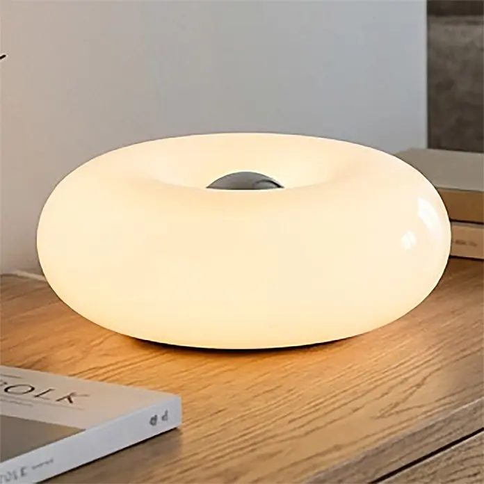Eglo LED-Tischleuchte rund Basile - 8 W, Ø x H: 30 x 12 cm, Weiß, Warmweiß - Leuchtende, mattweiße, donut-förmige Tischlampe strahlt warmes Licht auf einer Holzoberfläche aus.