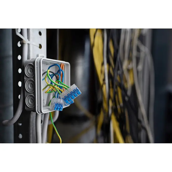 Ideal Hebelklemme 2/3/5-fach Gen II Kombipack - 30 Stk. - Offene elektrische Abzweigdose mit bunten Kabeln und blauen Hebelklemmen, auf einer Metallschiene zwischen weiteren Kabeln.