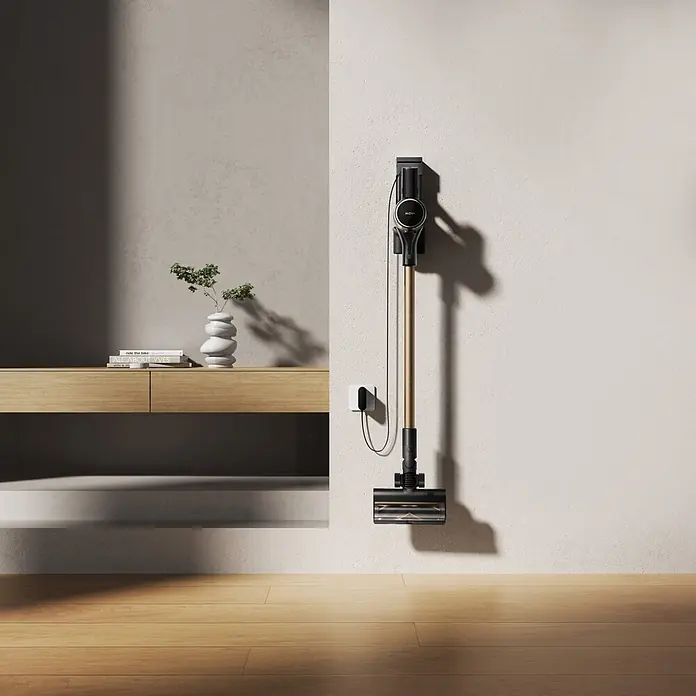Mova Aspirador de batería S5 Sense - 570 W, Volumen de recipiente: 0,6 l - Aspiradora de barra dorada y negra montada en pared clara, enchufada a una unidad de carga blanca. A la izquierda hay una consola de madera.