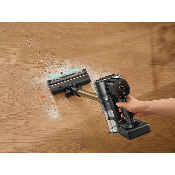 Mova Aspirador de batería S5 Sense - 570 W, Volumen de recipiente: 0,6 l - Un aspirador escoba inalámbrico negro y dorado con pantalla digital limpia suciedad de un suelo de madera, sujetado por una mano.