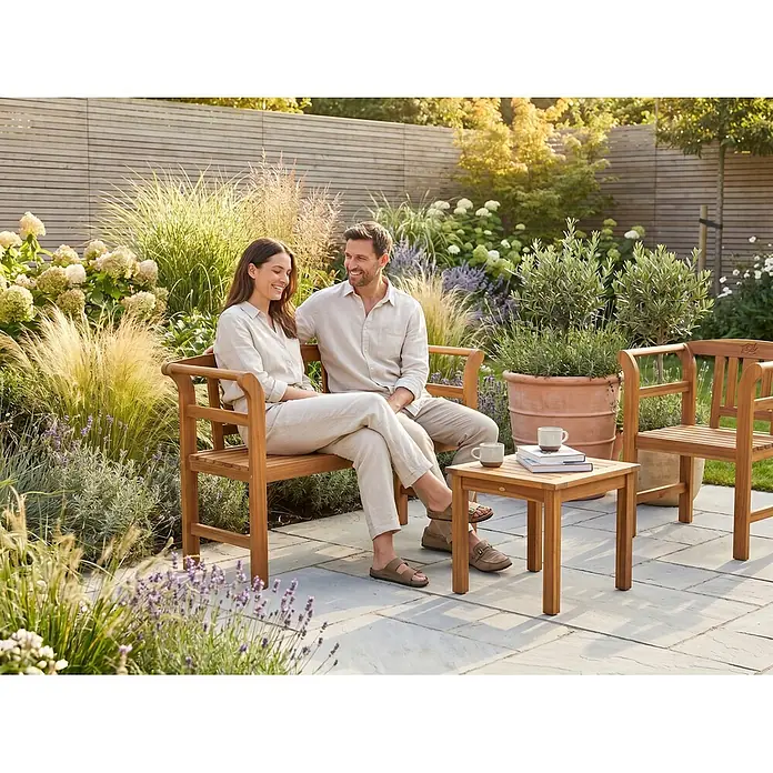 Prestige Home Living Outdoor Gartenbank Rose - B x T x H: 163 x 63 x 91 cm, Akazie, Braun - Sitzgruppe aus Holz für den Garten: Bank, Beistelltisch und Stuhl auf einer Terrasse, von einem Paar genutzt.