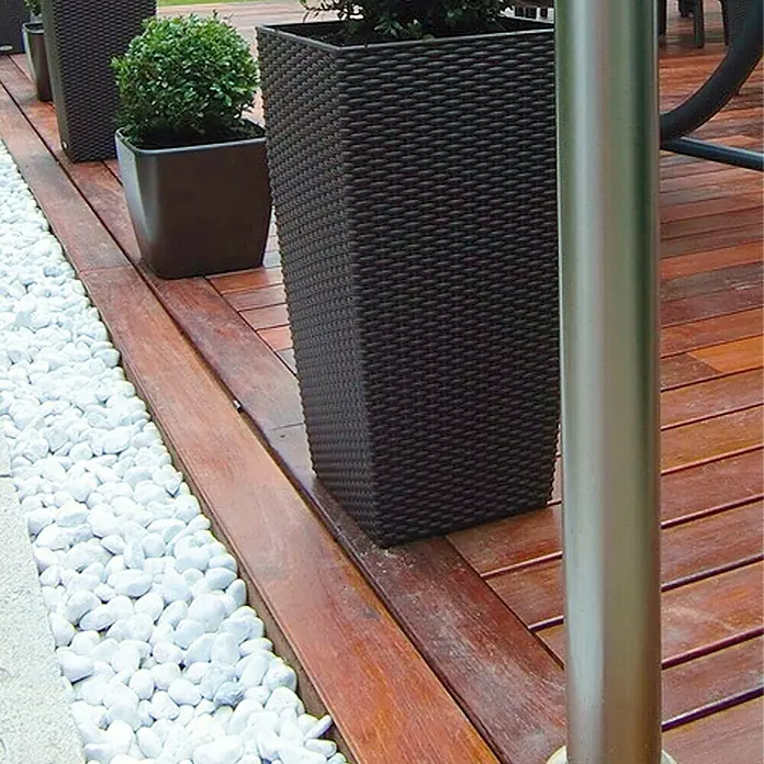 Min2C Marmorkiesel - Weiß, Körnung: 40 mm - 60 mm, 25 kg - Ein stilvoller dunkler Pflanzkübel auf einer Holzterrasse, umgeben von weißen Ziersteinen. Der Pflanzkübel bietet Platz für Pflanzen und Blumen.