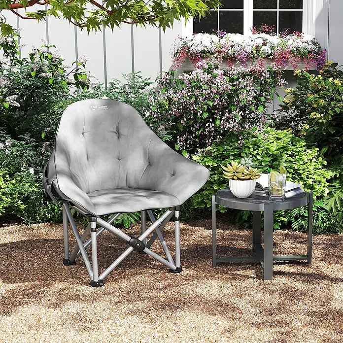 Outsunny Campingstuhl - Kunstleder, Metall, Klappbar, Dunkelgrau, B x T x H: 63 x 63 x 100 cm - Grauer gepolsterter Klappstuhl und passender grauer Beistelltisch in einem üppigen Garten, mit Getränk und Pflanze auf dem Tisch.