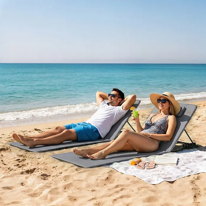 Outsunny Gartenliegen-Set - B x T: 57 x 154 cm, Dunkelgrau, Stahl, Klappbar - Zwei graue, tragbare Strandliegen mit Kopfstützen, genutzt von Personen, die an einem Sandstrand am Meer entspannen.