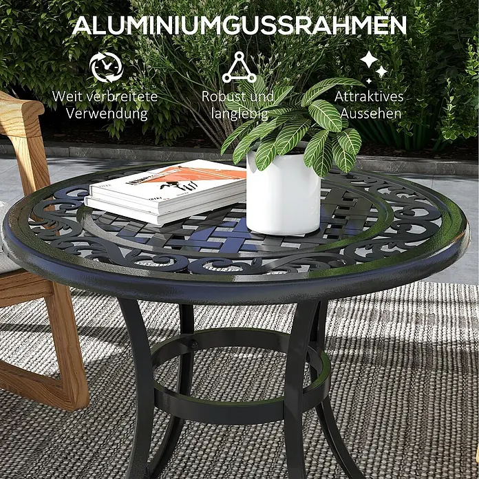 Outsunny Garten-Beistelltisch rund - Aluminiumguss, Schwarz - Runder, schwarzer Gartentisch aus Aluminiumguss mit verzierter Platte, auf einer Terrasse mit Buch und Pflanze, neben einem Holzstuhl.