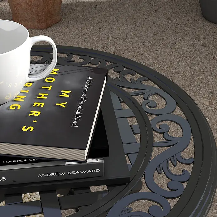 Outsunny Garten-Beistelltisch rund - Aluminiumguss, Schwarz - Dunkler, runder Outdoor-Metalltisch mit verschnörkelten Verzierungen, auf dem eine weiße Tasse und Bücher liegen.