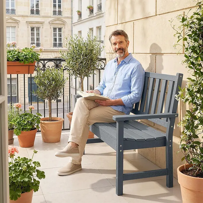 Outsunny Gartenbank - HDPE, Grau - Ein Mann liest auf einer grauen Gartenbank auf einem Balkon. Die robuste Bank fügt sich gut in die Außenumgebung ein.