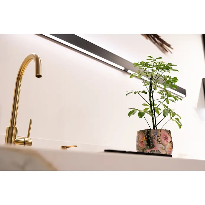 Ter Steege Übertopf rund Monstera Mystery - Ø x H: 21 x 21 cm, Metall, Grün - Moderner goldener Küchenhahn auf einer Arbeitsplatte, neben einer grünen Pflanze in einem Blumentopf, mit einer linearen Leuchte darüber.