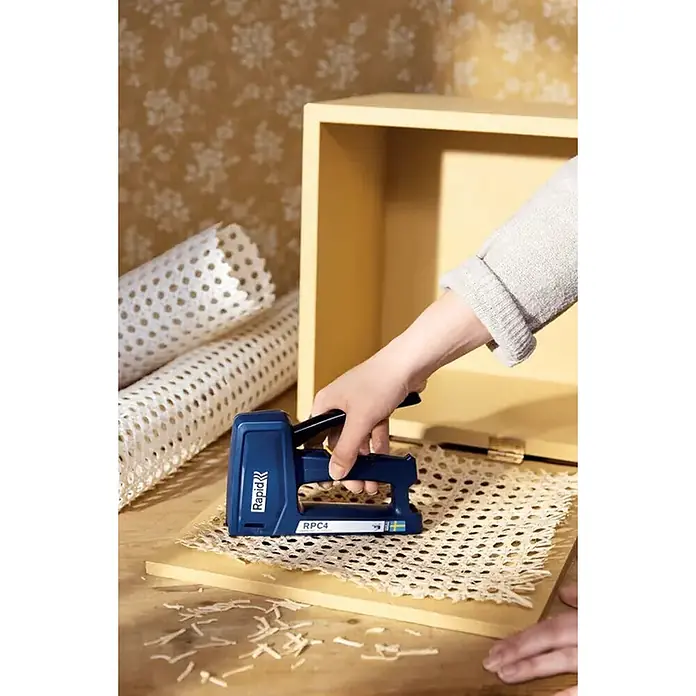 Rapid Grapadora manual RPC4 - Profundidad de grapado: 6 mm - 16 mm, Apto para: Papel - Una persona usa una grapadora azul Rapid RPC4 para fijar rejilla de caña a una tabla de madera clara.