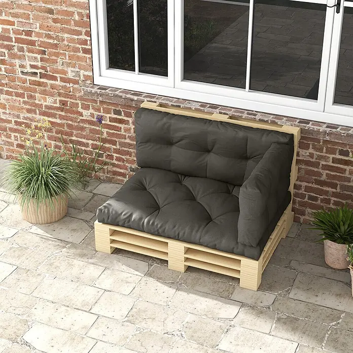 Outsunny Bankauflage - Dekopaletten, 1 Stk., 100% Polyester, Dunkelgrau - Outdoor-Ecksofa aus hellen Holzpaletten mit dunkelgrauen Kissen, als Sitzgelegenheit auf einer Terrasse vor einer Backsteinwand.