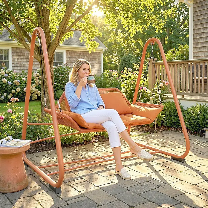 Outsunny Garten-Schaukelstuhl - 1 Stk., Metall, Polyester, Polypropylen Baumwolle, Schaumstoff, Terrakotta - Terrakotta-Gartenschaukel mit geflochtenen Details und orangefarbenen Kissen, auf der eine Frau entspannt.