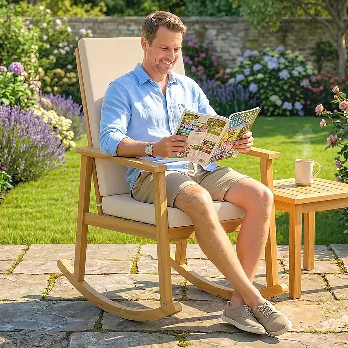 Outsunny Garten-Schaukelstuhl - 1 Stk., Akazienholz, Polyester, Beige - Hölzerner Schaukelstuhl mit cremefarbenen Kissen und Beistelltisch in einem Garten, mit einem Mann, der entspannt ein Magazin liest.