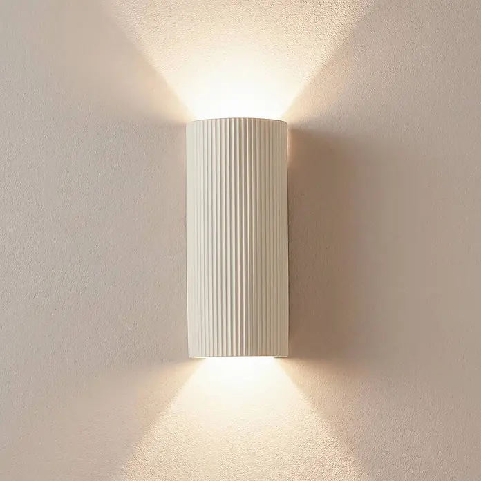Lindby Wandleuchte Colja - creme / amber, creme / amber, GU10 - Weiße gerippte zylindrische Wandleuchte, die warmes Licht nach oben und unten an eine strukturierte Wand wirft.