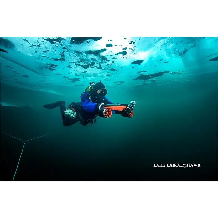 Sublue Tauchscooter Navbow 2026 - L x B x H: 486 x 327 x 177 mm - Taucher in blauem Trockenanzug nutzt orange-schwarzen Unterwasser-Scooter unter Eis im Baikalsee.