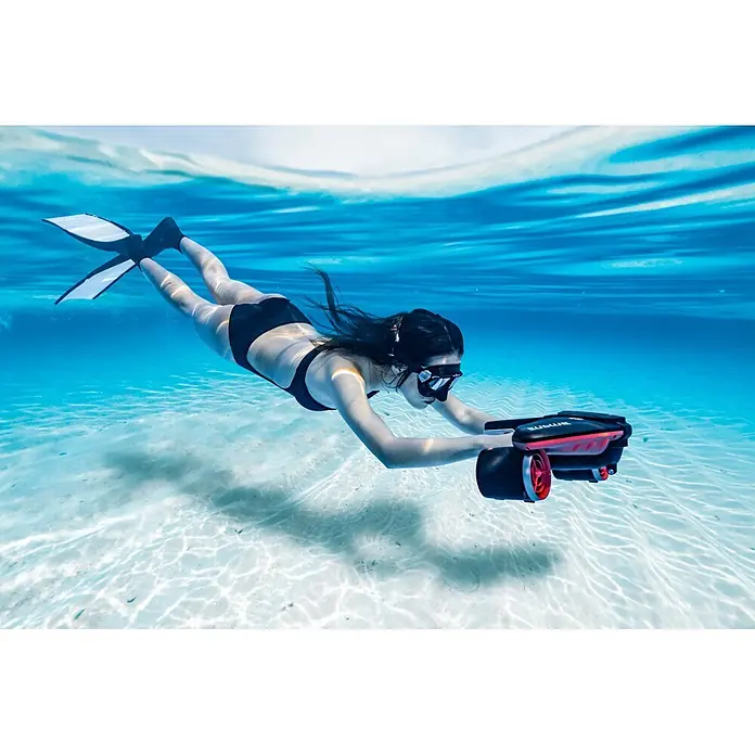 Sublue Tauchscooter Navbow 2026 - L x B x H: 486 x 327 x 177 mm - Person in schwarzem Badeanzug und Flossen, schnorchelnd mit einem rot-schwarzen SUBLUE Unterwasserscooter im klaren blauen Wasser.