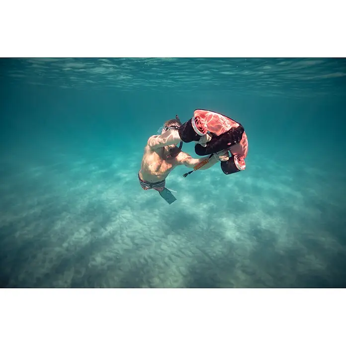 Sublue Tauchscooter Navbow 2026 - L x B x H: 486 x 327 x 177 mm - Person schnorchelt mit einem rot-schwarzen Unterwasser-Seascooter in klarem blauen Wasser.