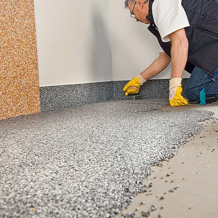 Probau Steinchenteppich Marmorkiesel, 2-4 mm - Grau, 20 kg - Ein Handwerker, der einen modernen Epoxidharzboden mit dekorativen Steinen verlegt. Der Boden wirkt robust und stilvoll.