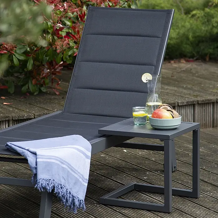 Happy Garden Garten-Beistelltisch BARBADOS - Aluminium, Quadratisch, Anthrazitgrau - Dunkelgraue Outdoor-Chaiselongue mit blauem Handtuch und passendem Beistelltisch mit Getränken und Obst auf einer Holzterrasse.