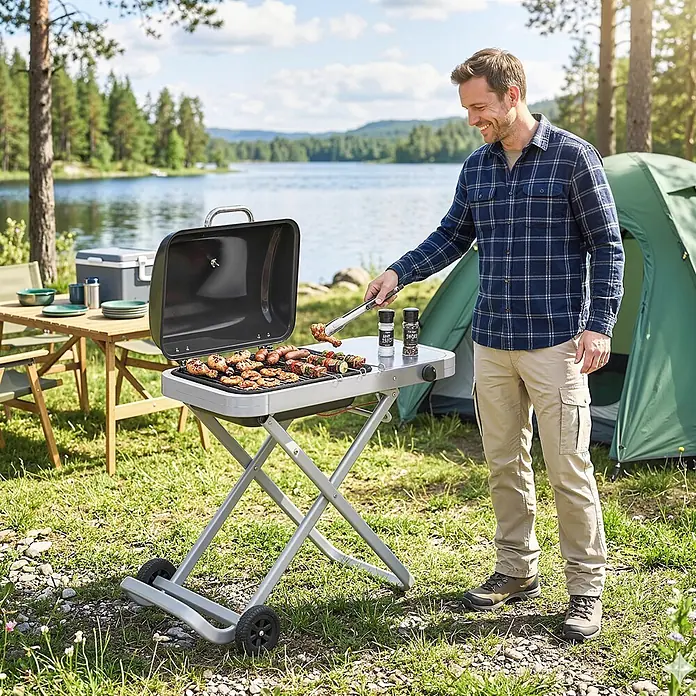 Outsunny Gasgrill - 2,5 kW, Anzahl Brenner: 1 Stk. - Ein Mann grillt auf einem grauen tragbaren Grill mit schwarzem Deckel am See, ideal für Camping.