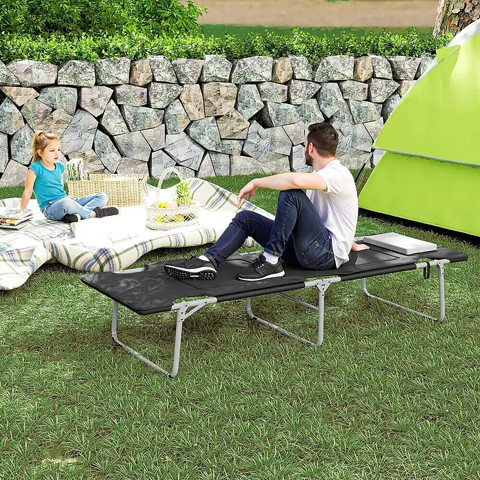 Outsunny Campingliege - Schwarz, Silber, B x T: 66 x 183 cm, Stahl, Klappbar - Ein Mann sitzt auf einem schwarzen, tragbaren Feldbett im Freien, was seine Nutzung demonstriert.