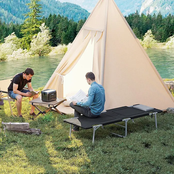 Outsunny Campingliege - Schwarz, Silber, B x T: 66 x 183 cm, Stahl, Klappbar - Zwei Männer campen am See. Einer liest auf einem schwarzen Campingliege, der andere an einem Holztisch mit einer dunkelgrauen Powerstation.