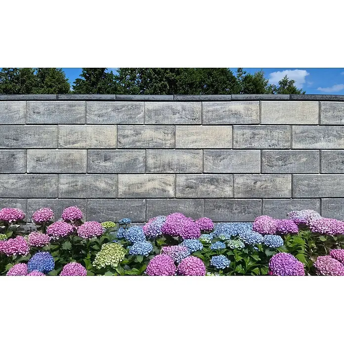Diephaus Mauerstein Lima - 40 x 20 x 20 cm, Graphit, Beton - Texturierte graue Beton-Stützmauerblöcke, mit blühenden Hortensien davor und Bäumen dahinter.