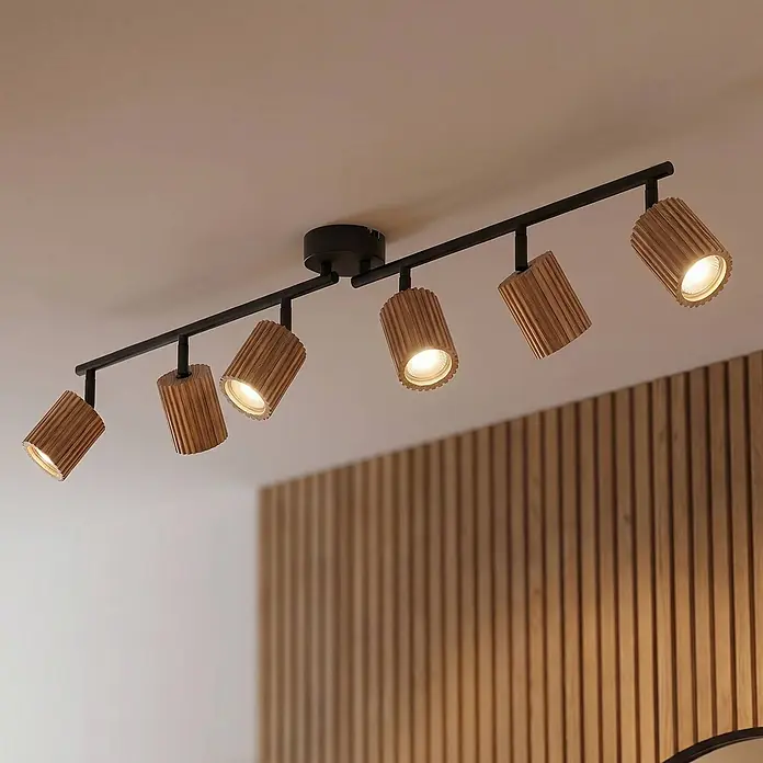 Lindby Deckenstrahler Stralino - L x B x H: 101,6 x 9 x 18,5 cm, Holz hell, GU10 - Schwarze Stromschiene mit sechs geriffelten Holzstrahlern, die einen Raum mit einer Holzlamellenwand beleuchten.