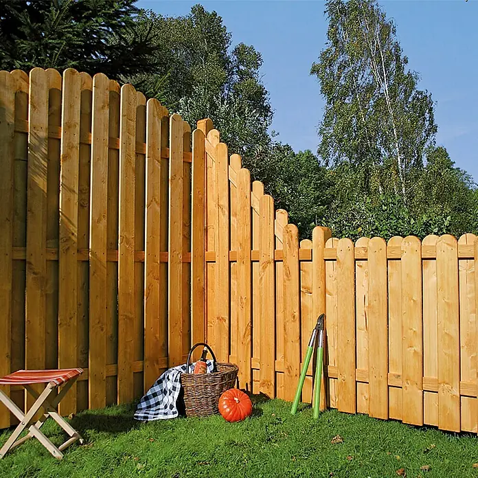 Sichtschutzelement Starnberg - 90 x 100/180 cm, Abgeschrägt, Herbstgold - Ein hellbrauner Holzzaun umrahmt einen Garten mit grüner Wiese, einem Kürbis und Gartenwerkzeug, perfekt für die Gartensaison.