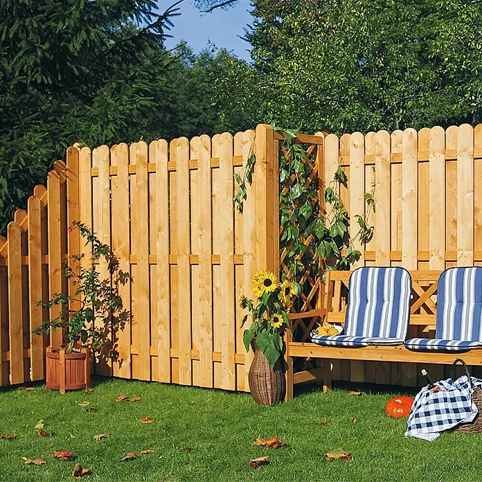 Sichtschutzelement Starnberg - 180 x 180 cm, Herbstgold - Holzzaun mit abgerundeten Spitzen, der einen Garten mit Bank, Blumen und Herbstdekorationen umgibt.