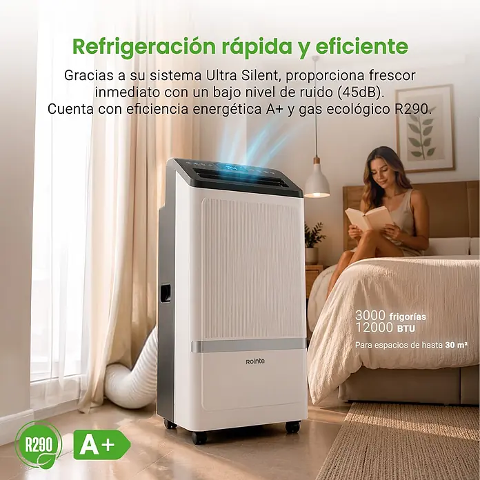 Rointe Aire acondicionado portátil Alghero 3000 - 3.000 W, Tamaño de la estancia: 20 m² - 30 m², Blanco - Aire acondicionado portátil blanco y gris con pantalla digital, enfriando un dormitorio moderno donde una mujer lee en la cama.