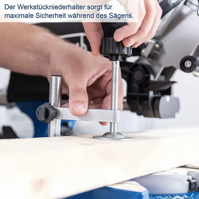 Scheppach Kappzugsäge HM216 - 2.000 W, Durchmesser Sägeblatt: 216 mm, Leerlaufdrehzahl: 4.700 U/min - Ein silberner Werkstückniederhalter mit schwarzem Drehknopf sichert ein Holzbrett auf einer Kappsäge. Eine Hand justiert ihn für sicheren Betrieb.