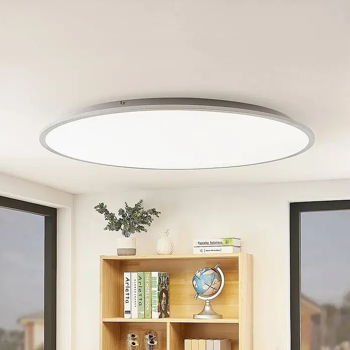 Lindby Deckenleuchte Narima - L x B x H: 100 x 100 x 5,2 cm, alu / grau / zink, weiß / opal - Runde LED-Deckenleuchte mit silbernem Rahmen und weißem Diffusor, die einen Raum beleuchtet.