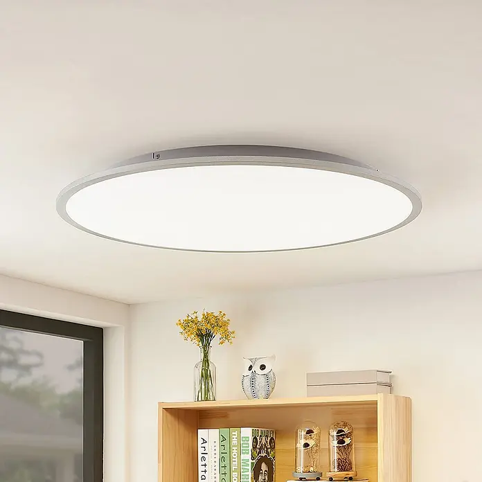 Lindby Deckenleuchte Narima - alu / grau / zink - Runde LED-Deckenleuchte mit grauem Rahmen und weißer Abdeckung, an einer Decke über einem Bücherregal montiert.